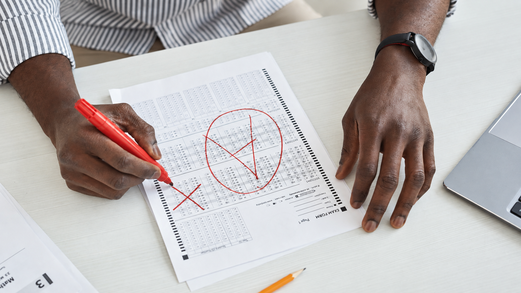 Hands marking an assessment answer sheet with a red pen